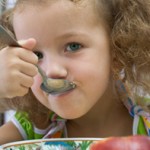 The girl has breakfast corn flakes with milk, over white